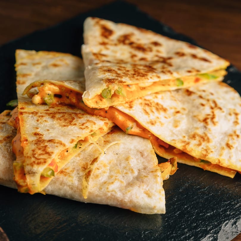 Several golden-brown quesadilla wedges with melted cheese and green peppers on a dark slate board.
