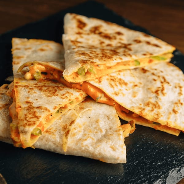 Several golden-brown Metztli Mexican Taqueria quesadilla slices with melted cheese and green peppers on a dark plate.
