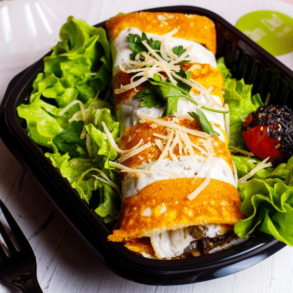 Mexican enchiladas topped with sour cream, cheese, and parsley, served with lettuce and a tomato.